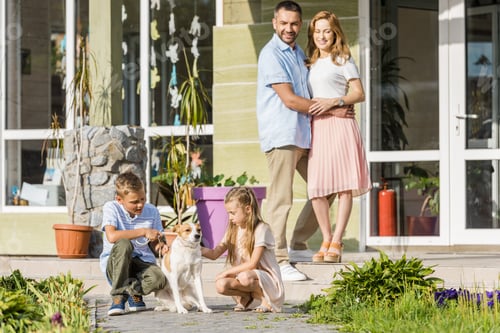 Preview: happy parents looking at children playing with dog outside house