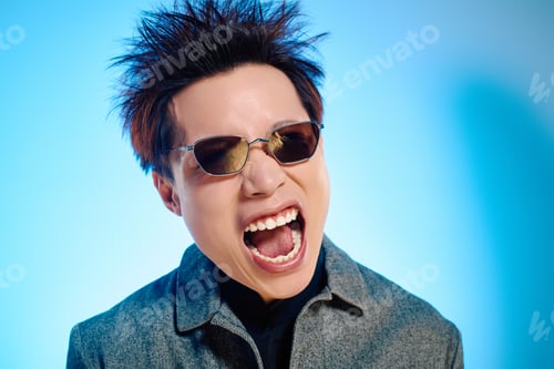 Preview: Stylish Asian man excitedly poses against a vibrant blue background in a photoshoot