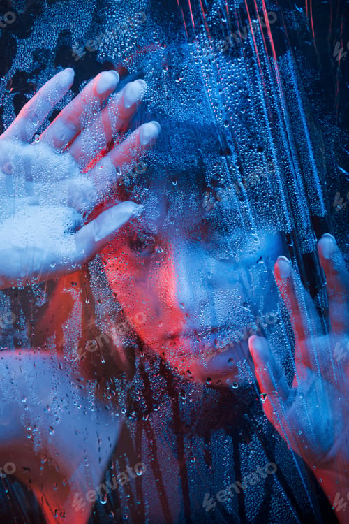 Preview: Studio shot in dark studio with neon light. Portrait of beautiful woman behind wet glass