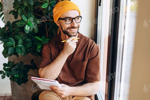 Preview: Portrait of handsome, happy, bearded man wearing stylish eyeglasses and yellow hat taking notes