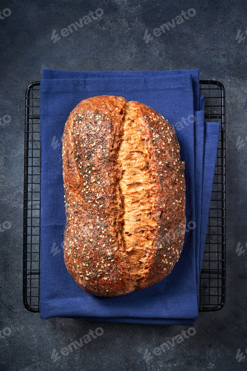 Preview: Fresh homemade artisan bread with seeds on dark gray surface.