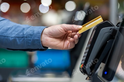 Preview: Cropped of adult humans hand placing gold credit card on pos terminal of supermarket during