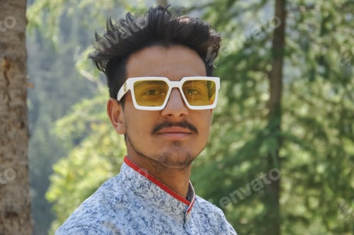 Preview: Closeup of a good looking young guy standing outdoor in the nature and wearing sunglasses