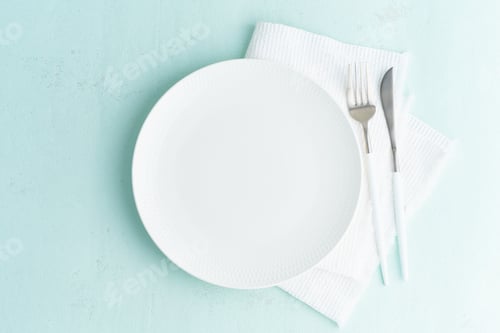 Preview: Clean empty white plate, fork and knife on green blue turquoise stone table, copy space, mock up