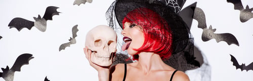 Preview: panoramic shot of girl in black witch Halloween costume with red hair licking skull near white wall