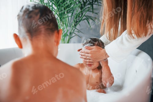 Preview: Having fun. Young mother helps her son and daughter. Two kids washing in the bath