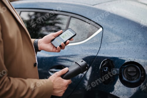Preview: Close up of businessman using electric vehicle charging app, checking charging of his electric car.