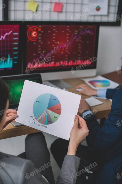 Preview: Cropped view of information security analyst holding paper with chart near colleague using computer