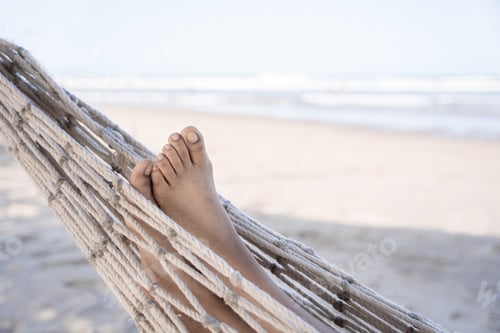Preview: A close-up of a young Hispanic woman's sandy feet as she lounges on a hammock at the beach.