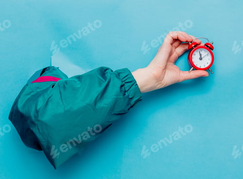 Preview: Female hand in 90s style jacket holding alarm clock