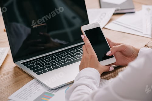 Preview: cropped shot of businesswoman using smartphone at workpalce with laptop