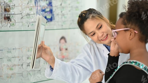 Preview: Smiling optician helping child girl choosing the most appropriate eyeglasses.