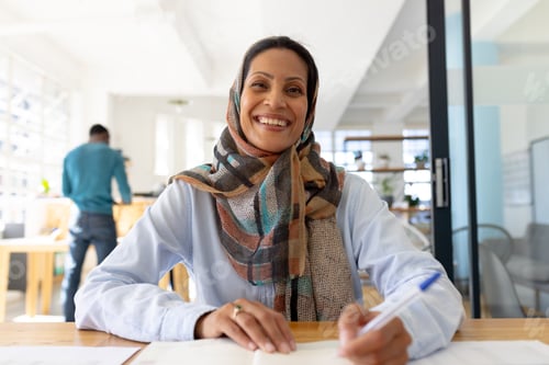 Preview: Portrait of happy muslim biracial businesswoman in headscarf looking at camera in modern office