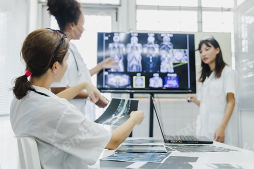 Preview: Team of female doctor check on scan results paper and looking at monitors in laboratory