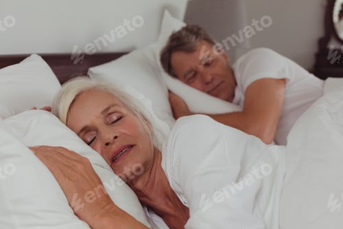 Preview: Side view of active senior Caucasian couple sleeping together in bed in bedroom at comfortable home