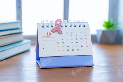 Preview: A calendar is open to the month of October, with a pink awareness ribbon placed on it.