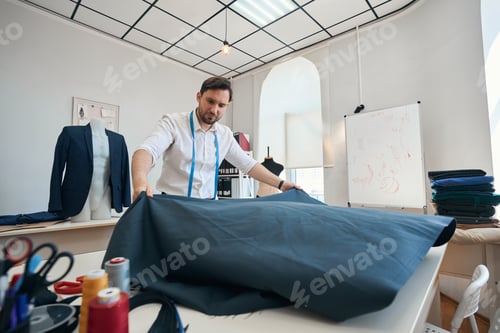 Preview: Man couturier laid out black cloth on large white table