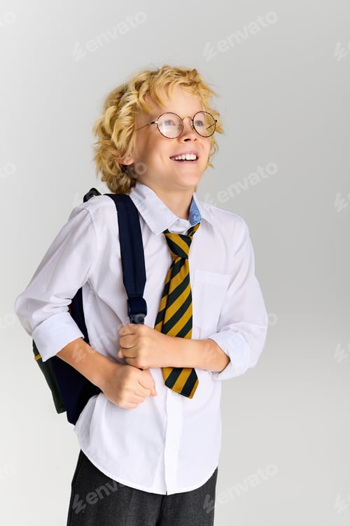 Preview: Blonde boy in school uniform smiles brightly in studio setting with backpack