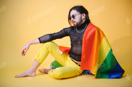 Preview: gay man with a gay pride flag smiling and looking away on yellow background