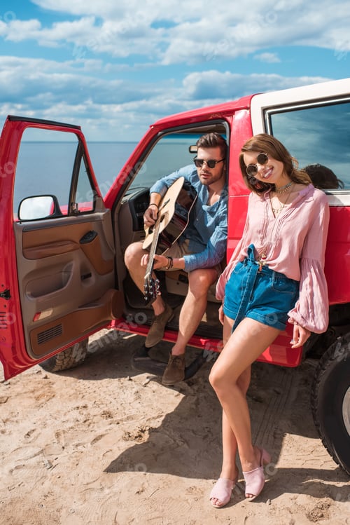 Preview: young couple with acoustic guitar near car on road trip