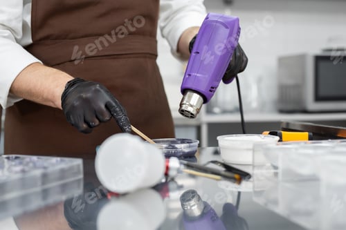Preview: Male pastry chef heats the chocolate glaze with a construction hair dryer