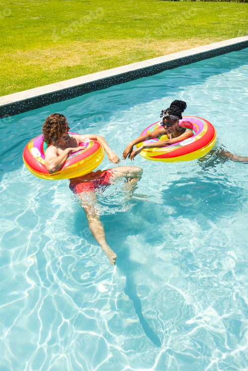 Preview: Diverse couple young Caucasian man and African American woman relax in pool floats with copy space