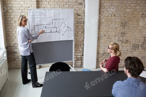 Preview: Mature businesswoman explaining floor plan to colleagues
