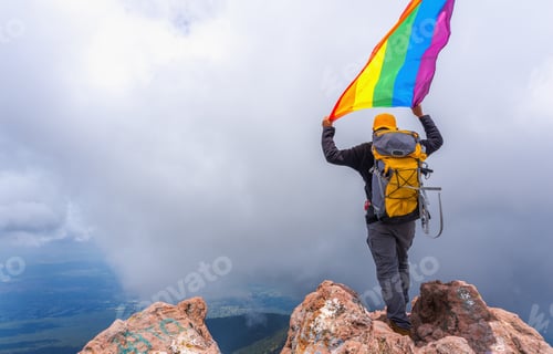 Preview: Hiker with a backpack standing on the top of the mountain and holding a pride flag