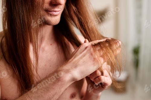 Preview: Hair care concept for men. A young guy looks at his hair, problems with men hair