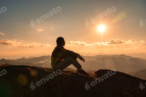 Preview: Silhouette young hiker woman relaxing and enjoying the sunset view on top of mountain peak
