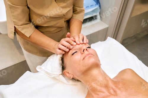 Preview: Middle aged woman enjoys hand anti-aging facial treatment massage in spa salon.