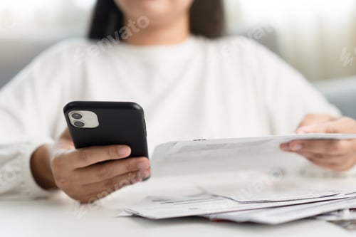 Preview: Woman holding paper bill invoice and mobile phone