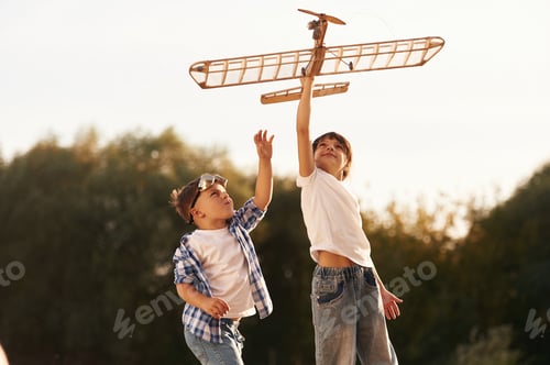 Preview: Boy and girl are playing with wooden toy plane on the field
