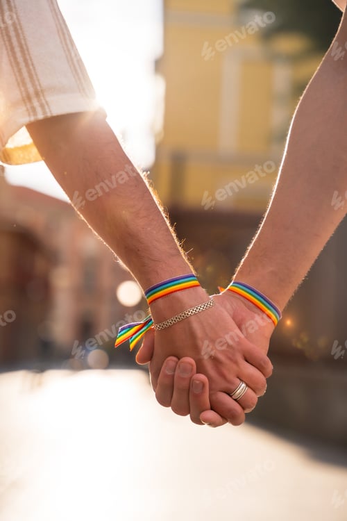 Preview: Detail of the holding hands of a couple of homosexual men with the rainbow flag at the pride