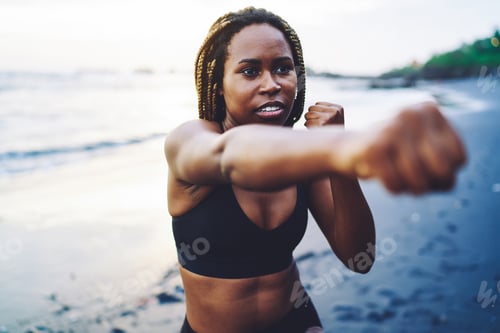 Preview: Motivated fit girl with dark skin practice boxing during morning workout at sea coast