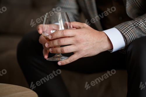Preview: A man businessman holds a glass with alcohol in his hand. Dressed in a jacket and shirt