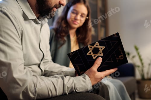 Preview: Focus on black cover of Torah with star of David in hands of bearded rabbi