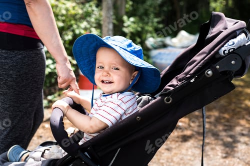 Preview: Smiling Toddler in Stroller Outdoors Wearing Blue Hat