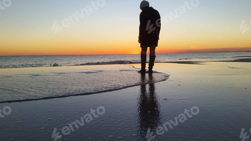 Preview: Silhouetted millennial woman deep in thought about her future at sunset on beach vacation at sea.