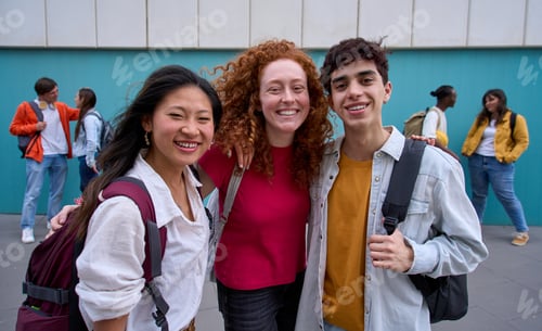 Preview: Group portrait of three smiling multiracial students hugging with backpacks looking at camera.