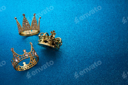 Preview: Epiphany Day or Dia de Reyes Magos concept. Three gold crowns on blue sparkling background