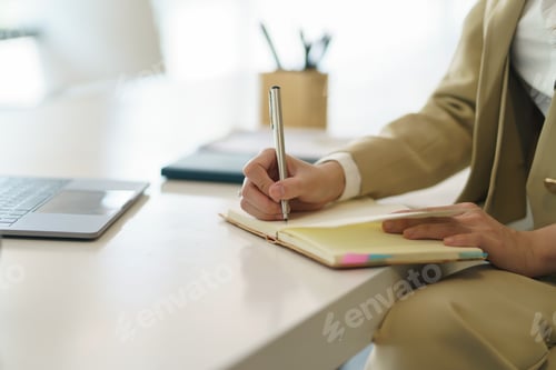 Preview: Closeup image of a woman writing and taking note on notebook with laptop in office.