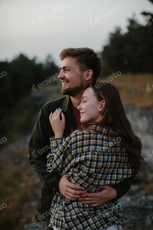 Aperçu: Un beau jeune homme et une jolie femme dans les bras l'un de l'autre profitent du coucher de soleil dans les montagnes