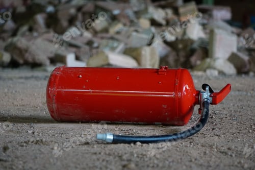 Preview: Vibrant red fire extinguisher situated among a pile of grey and white stones