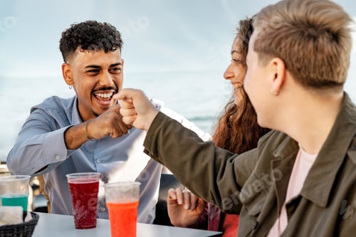 Preview: Friends sharing a celebratory fist bump at an outdoor seaside café