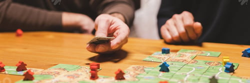 Preview: men friends have fun playing the carcassonne board game at night. male hands and game cards and chip