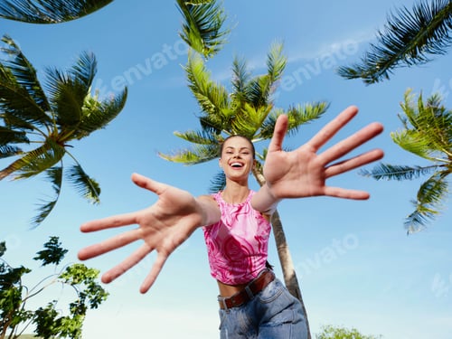 Preview: Woman, palm trees, blue sky a woman joyfully raises her hands against a backdrop of lush palm trees
