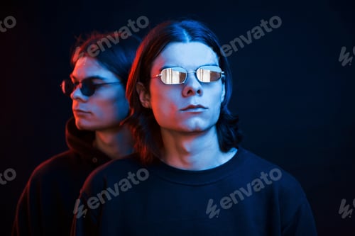Preview: Similar clothes. Portrait of twin brothers. Studio shot in dark studio with neon light