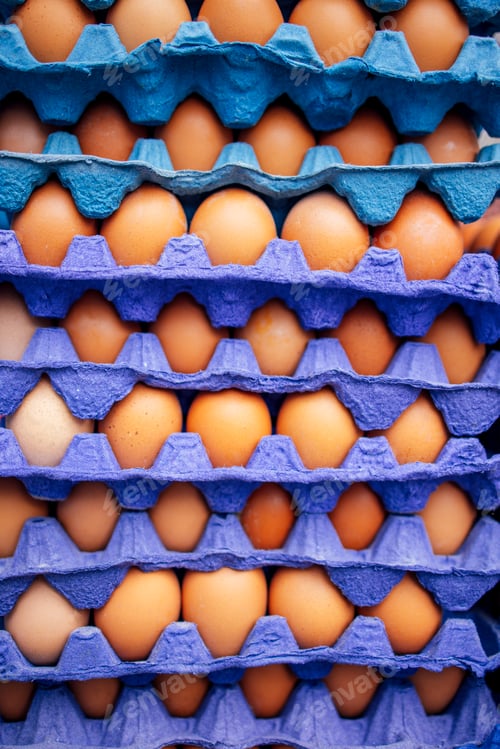 Preview: Stacked egg cartons filled with fresh brown eggs in vibrant blue and purple packaging