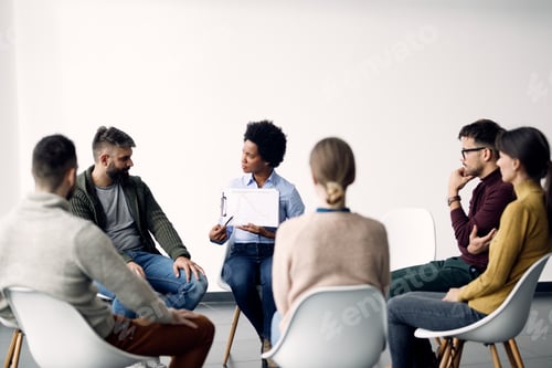 Preview: African American psychotherapist analyzing progress with group of people during a session.